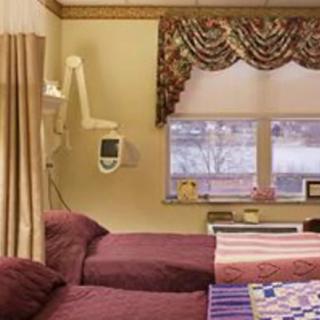 A hospital room with two beds and a window adorned with curtains.