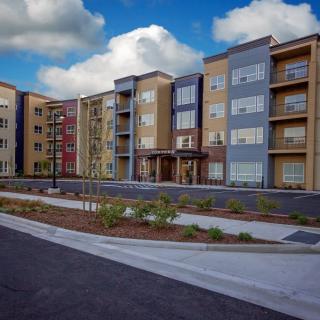 A modern multi-story apartment building with well-maintained landscaping under a blue sky.