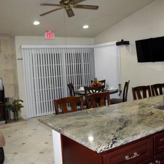 A modern kitchen with a dining area featuring a granite countertop, ceiling fan, and sliding doors with blinds.