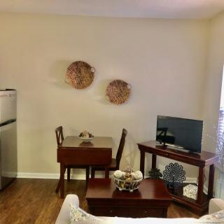 A cozy living room with minimalist decor, featuring a small dining table set and a TV on a wooden stand.