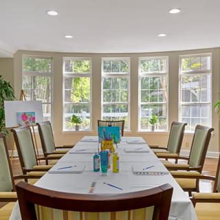 A well-lit conference room with a meeting table surrounded by chairs, set up with notepads and pens.