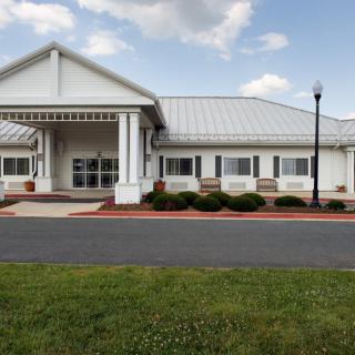A white building with a modern design featuring a prominent entrance, surrounded by well-kept landscaping and under a partly cloudy sky.
