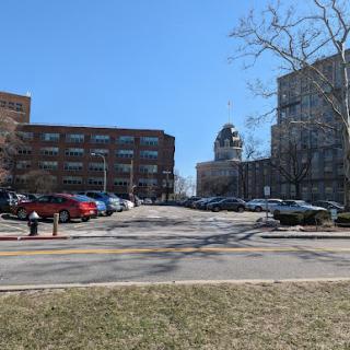 A view of a parking lot surrounded by modern buildings under a clear blue sky.