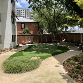 A well-maintained garden with a winding pathway, surrounded by trees and a wooden fence in an urban setting.