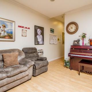 A cozy living room featuring a sofa and a piano, adorned with wall art and a decorative clock.