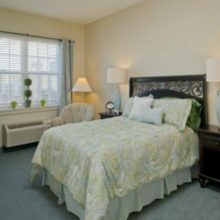 A cozy bedroom with a neatly made bed, nightstands, lamps, and a window with drapes.
