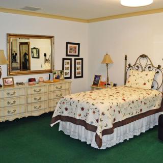 A cozy bedroom with a bed, dresser, and mirror. The room features warm lighting and decorative touches.