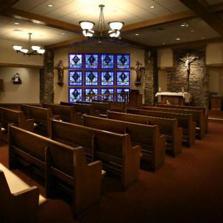 Interior of a chapel featuring wooden pews, stained glass windows, and an altar with a crucifix.