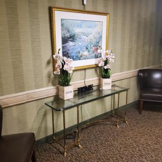 A well-decorated interior space featuring a glass table with potted flowers and a landscape painting above it.