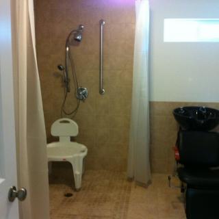 An accessible bathroom featuring a shower area with a chair, grab bars, and a handheld showerhead.