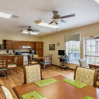 A communal kitchen and dining area with wooden tables and chairs, ceiling fans, and large windows.
