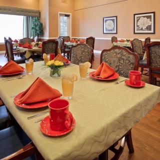 A warmly decorated dining room with a table set for a meal, featuring red dishware and orange napkins.