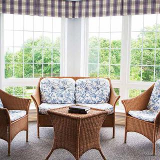 A cozy sunroom with wicker furniture and floral cushions, bathed in natural light.
