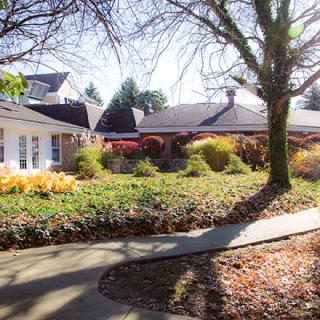 A residential home with a landscaped yard, featuring trees and an autumn pathway.