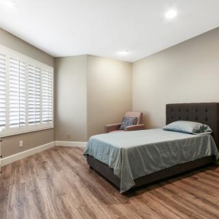 A minimalist bedroom with a neatly made bed and hardwood flooring.