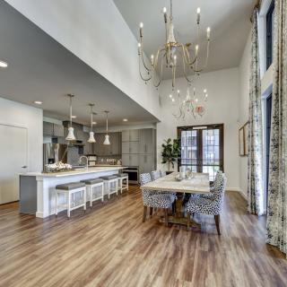 A spacious and modern open floor plan featuring a kitchen with bar stools and an elegant dining area, highlighted by wood flooring and a large chandelier.