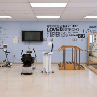 A physical therapy room equipped with exercise machines, parallel bars, and motivational quotes on the wall.