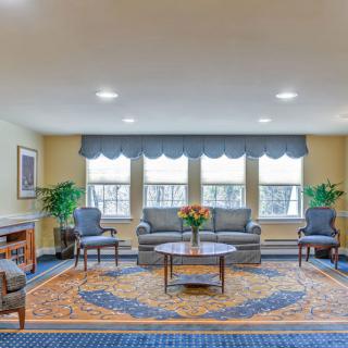 A well-lit living room with a sofa, chairs, and a central coffee table surrounded by windows.