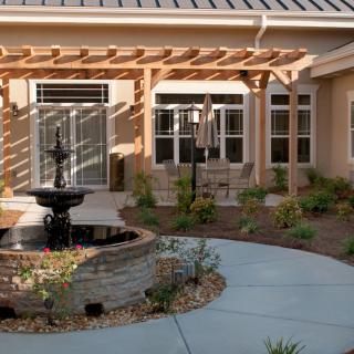 A serene courtyard featuring a central fountain, surrounded by a pergola and well-maintained garden landscaping.