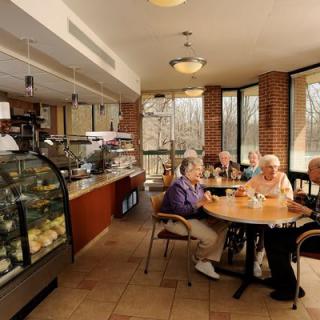 A group of seniors enjoying a conversation in a cozy cafe with a dessert display in the background.