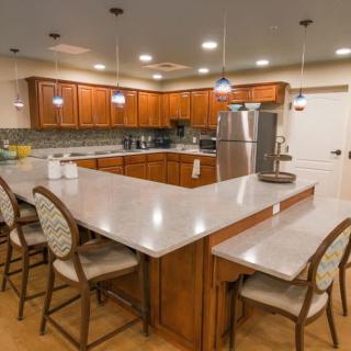 A modern kitchen with an island, wooden cabinets, stainless steel appliances, and bar stools.