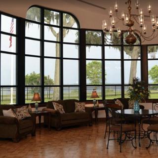 A spacious living room with large windows offering a scenic view, decorated with elegant furniture and a chandelier.
