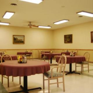 An empty dining area with several tables and chairs set up, illuminated by ceiling lights.