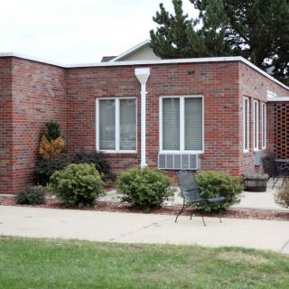 A brick house with large windows and a small patio area surrounded by greenery.