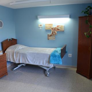 A hospital patient room featuring a bed, nightstand, and soothing blue walls.