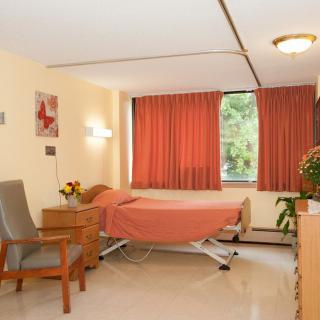 A tidy hospital room with a single bed, chair, and window with curtains.