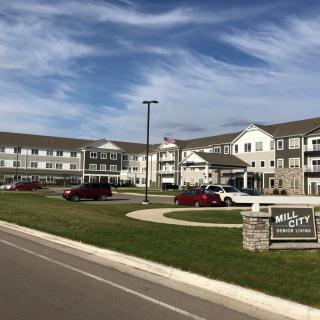 A large residential building with a parking lot and well-maintained lawn under a partly cloudy sky.