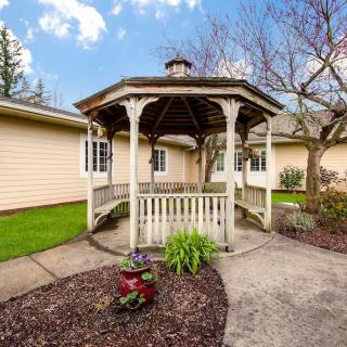 A charming gazebo in a well-maintained garden, surrounded by trees and adjacent to a house.