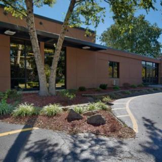 A brown brick building with large windows, surrounded by landscaped greenery and a curved driveway.