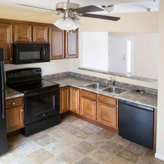 A modern kitchen with wood cabinets, black appliances, and a ceiling fan.