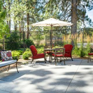 A cozy patio setup with red cushioned chairs surrounding a table under a large umbrella, nestled in a lush garden setting.