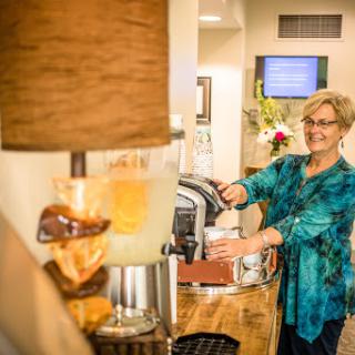 A cheerful woman prepares coffee at a cozy beverage station, illuminated by a stylish lamp.
