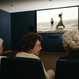A group of seniors watching a black and white movie in a theater.