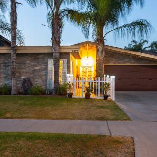 A suburban house in the evening with palm trees and a well-lit entrance.