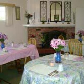 A cozy dining room with tables adorned with floral arrangements and a fireplace in the background.