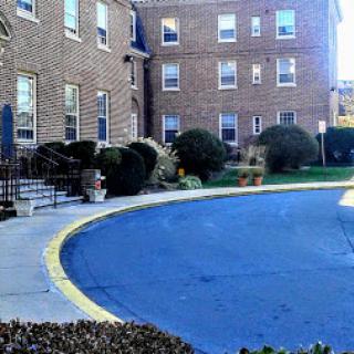 A view of a brick apartment building with a landscaped area and a curved driveway.