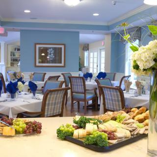 A beautifully set dining room with elegant tables and a tray of assorted sandwiches and fruits.