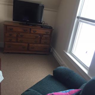 A cozy living room corner with a TV on a dresser, next to a comfortable chair and a large window.