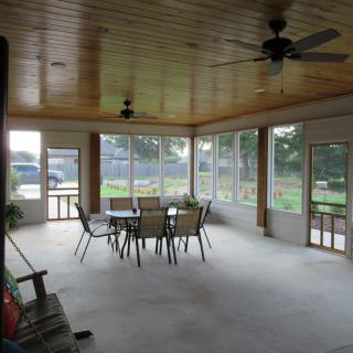 A spacious sunroom with a dining table and chairs, featuring large windows and ceiling fans.