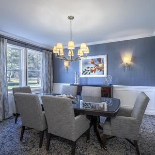 A well-furnished dining room with a chandelier and large windows.