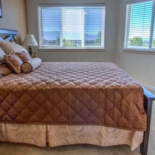 A cozy bedroom with a large bed and multiple windows, featuring a quilted bedspread and decorative pillows.