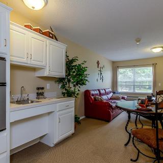 A cozy apartment interior with a kitchen area and a well-lit living room featuring comfortable furniture.