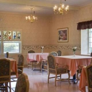 A cozy dining room with neatly arranged tables and chairs, illuminated by chandeliers.