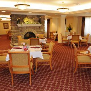 A cozy dining room interior with tables and chairs arranged around a fireplace.