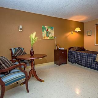 A cozy room featuring a bed, a set of chairs and a table, warmly lit with tasteful decor.