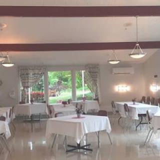 A spacious event room featuring neatly arranged tables and chairs, illuminated by soft lighting and natural light coming through the windows.